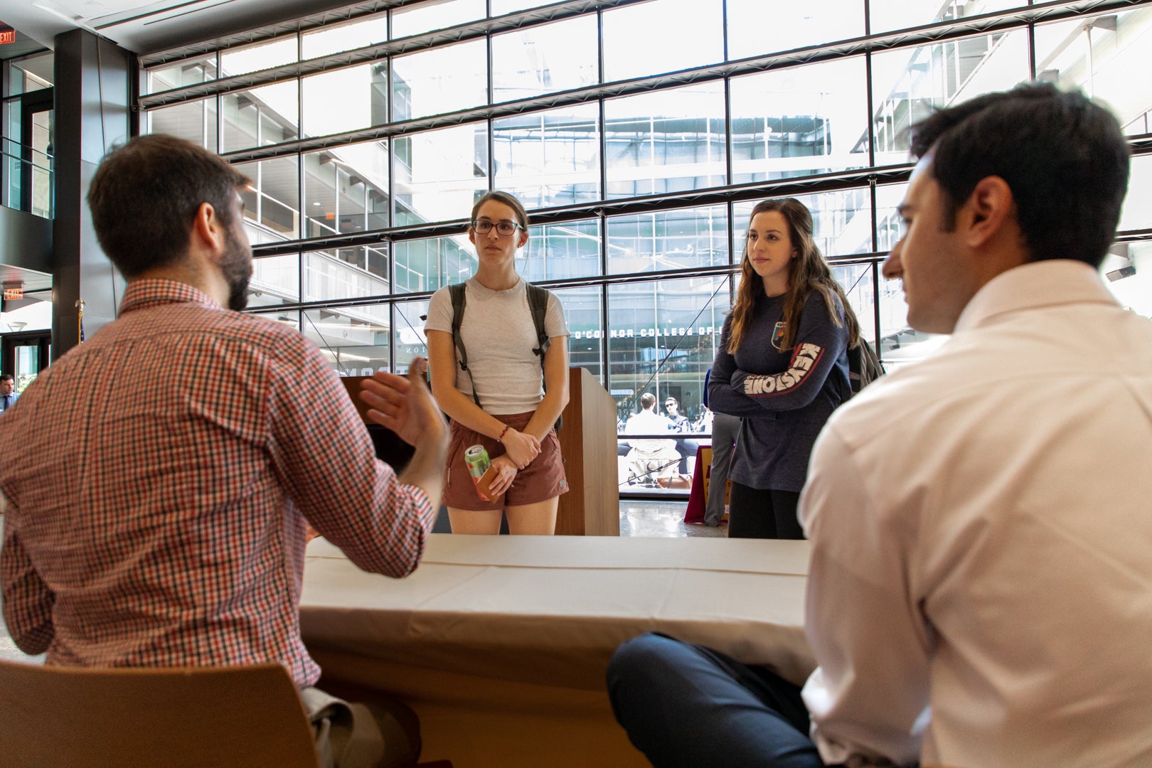 Two students talking to two professors in front of the windows in the W.P. Carey Foundation Armstrong Great Hall at ASU Law. 