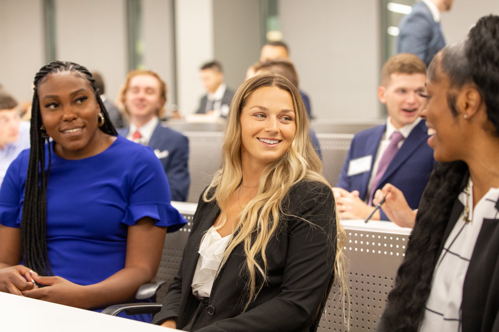 Three MSLB students talking at a classroom table surrounded by other students at the MSLB Fall Orientation.