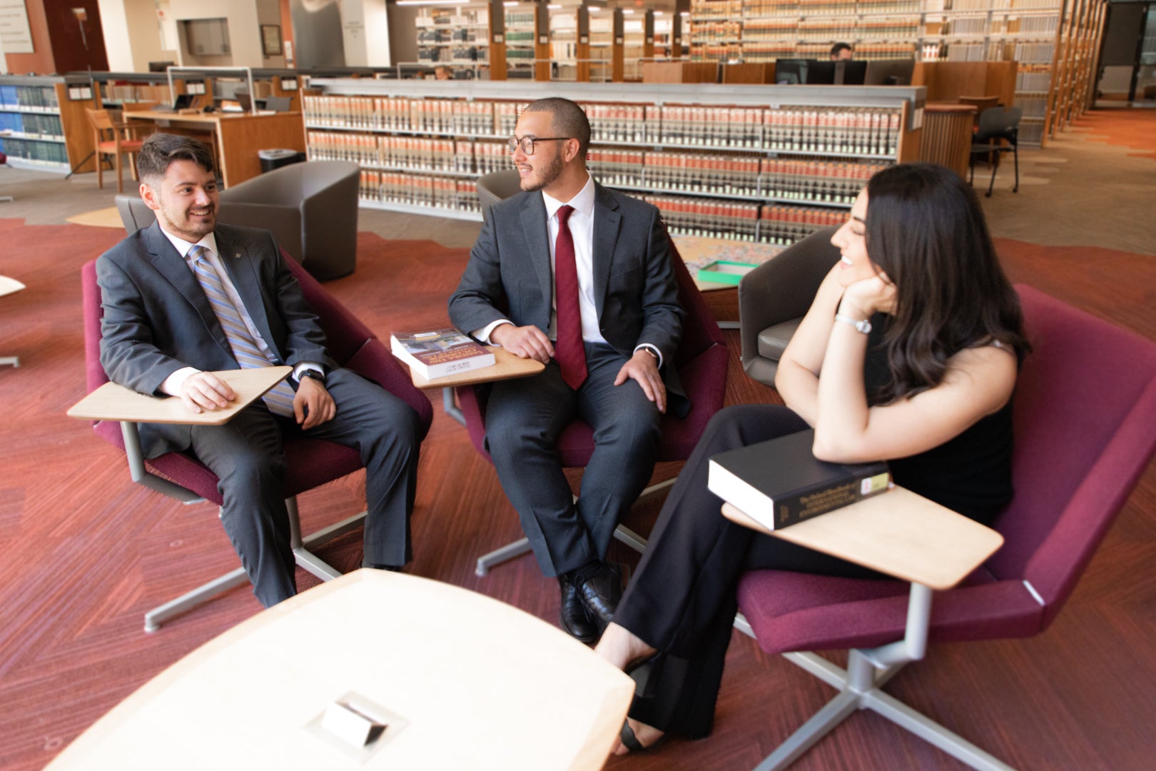 Three ASU Law student sitting and chatting in the Ross-Blakely Law Library on maroon library chairs.