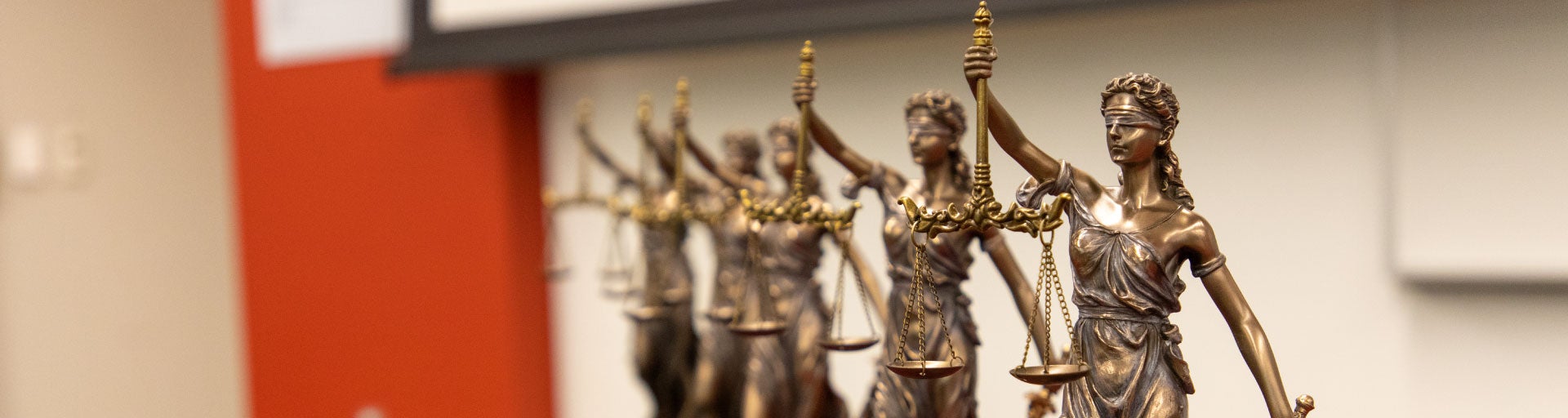 Five Lady Justice bronze statues displayed on a table in a row.
