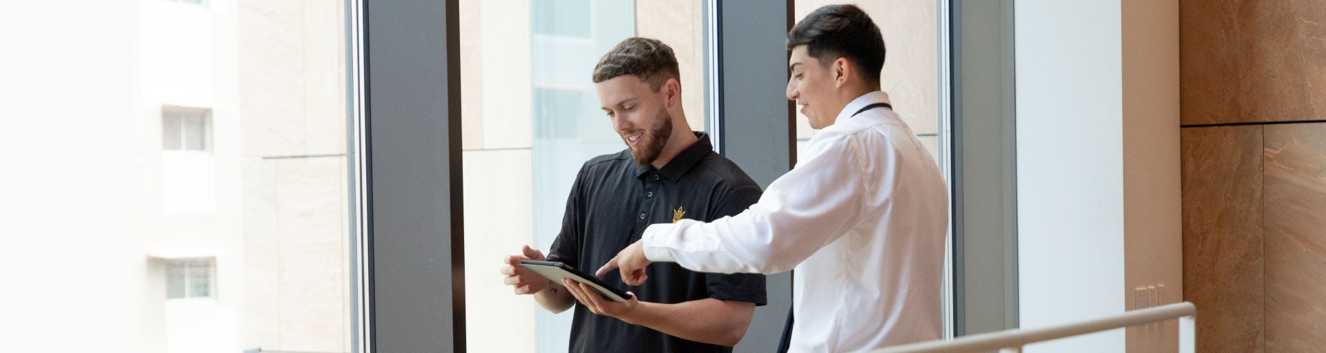 A student in white button-down shirt pointing at an open book that another student in a blue shirt is holding. They are in front of the ASU Law reading room windows.