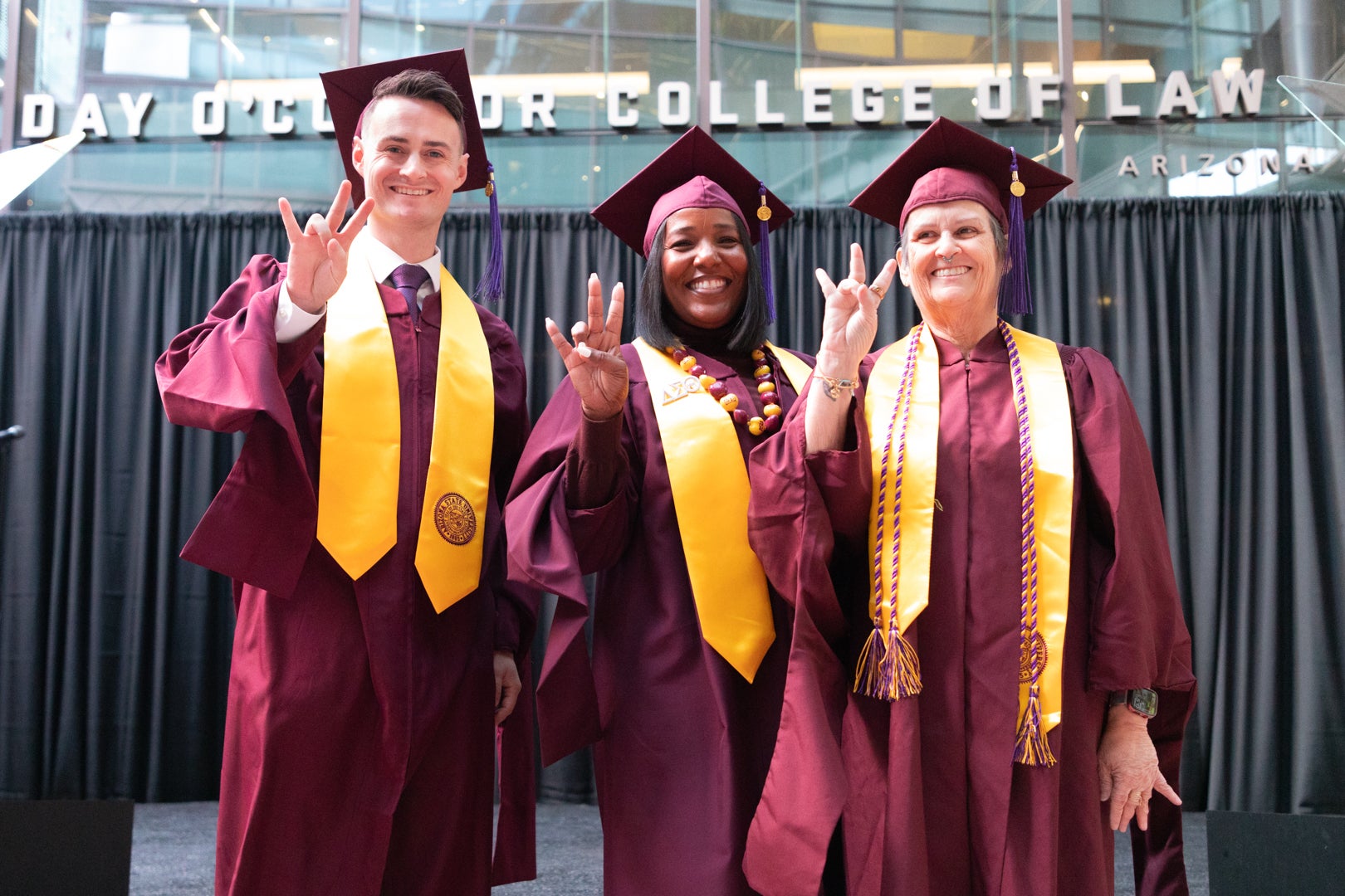 Three Masters of Legal Studies students holding up the pitchfork sign during the Fall 2023 Convocation Ceremony.