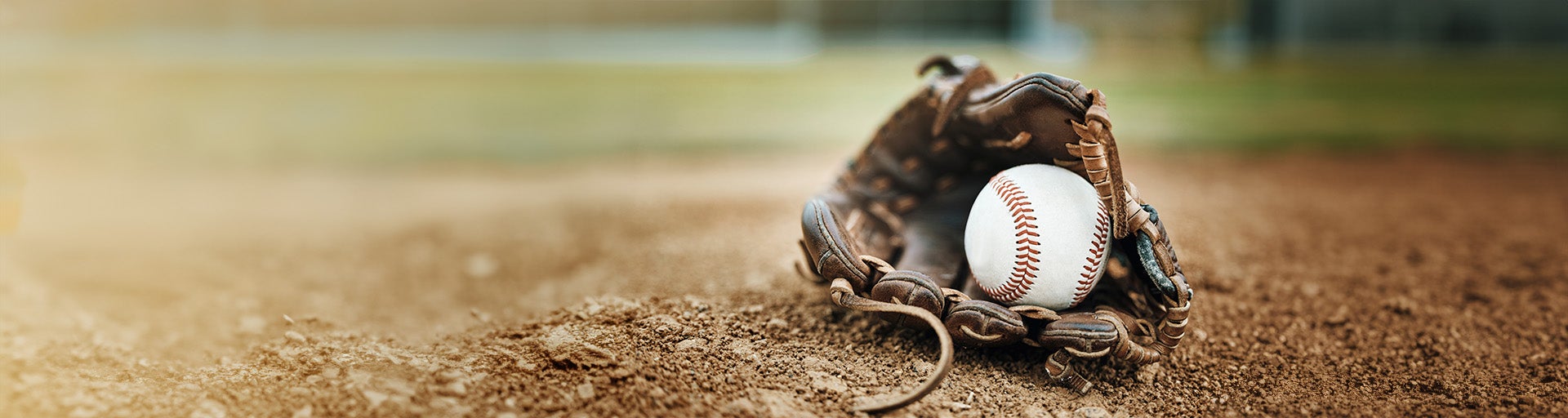 Brown baseball glove holding a white baseball placed on a baseball field.