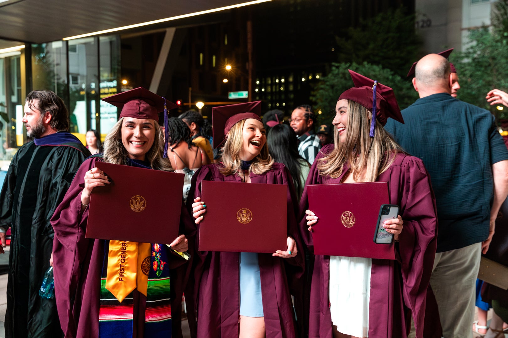 ASU Law graduates in maroon regalia smiling and laughing while holding up their ASU diploma. 
