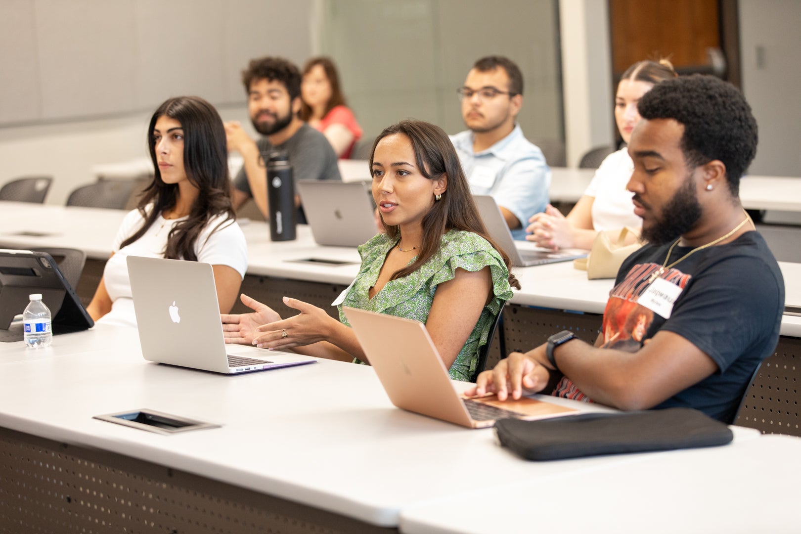 Three students sitting at a long desk in an ASU Law classroom. The woman in the middle is talking to someone at the front of the room.