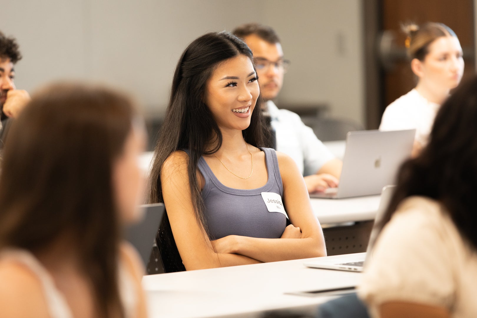 ASU student sitting at desk smiling while folding her arms and listening to someone talk at the front.