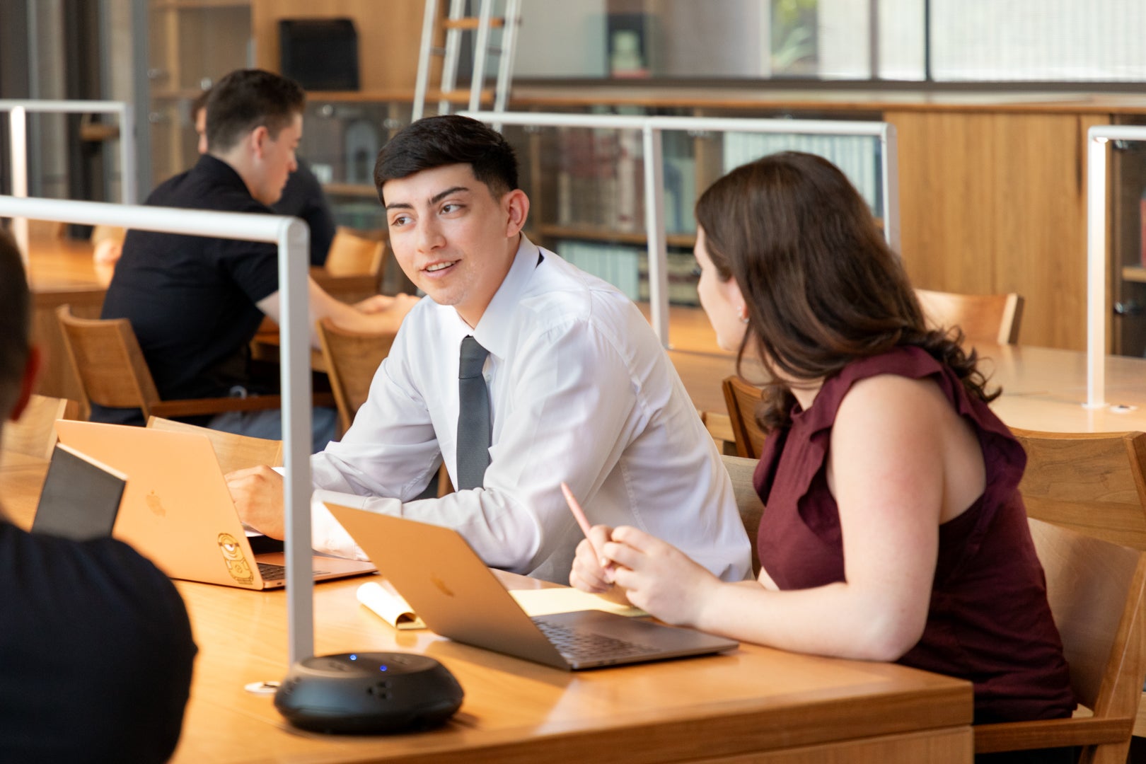 Two ASU Law students sitting at a table in the Reading Room talking while working on their laptops.