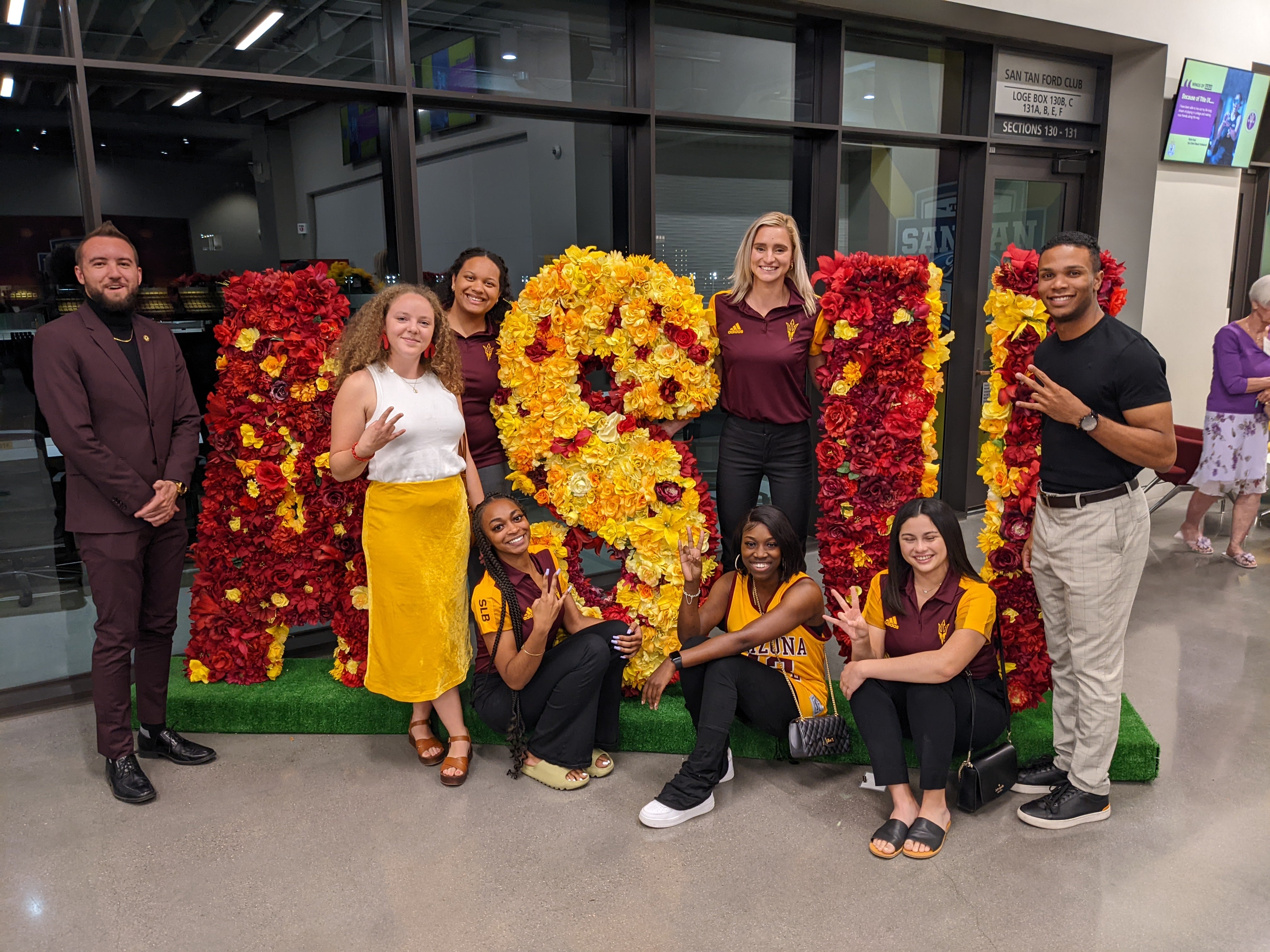 Sports Law and Business students holding up the ASU pitchfork in front of a 3D ASU floral sign.