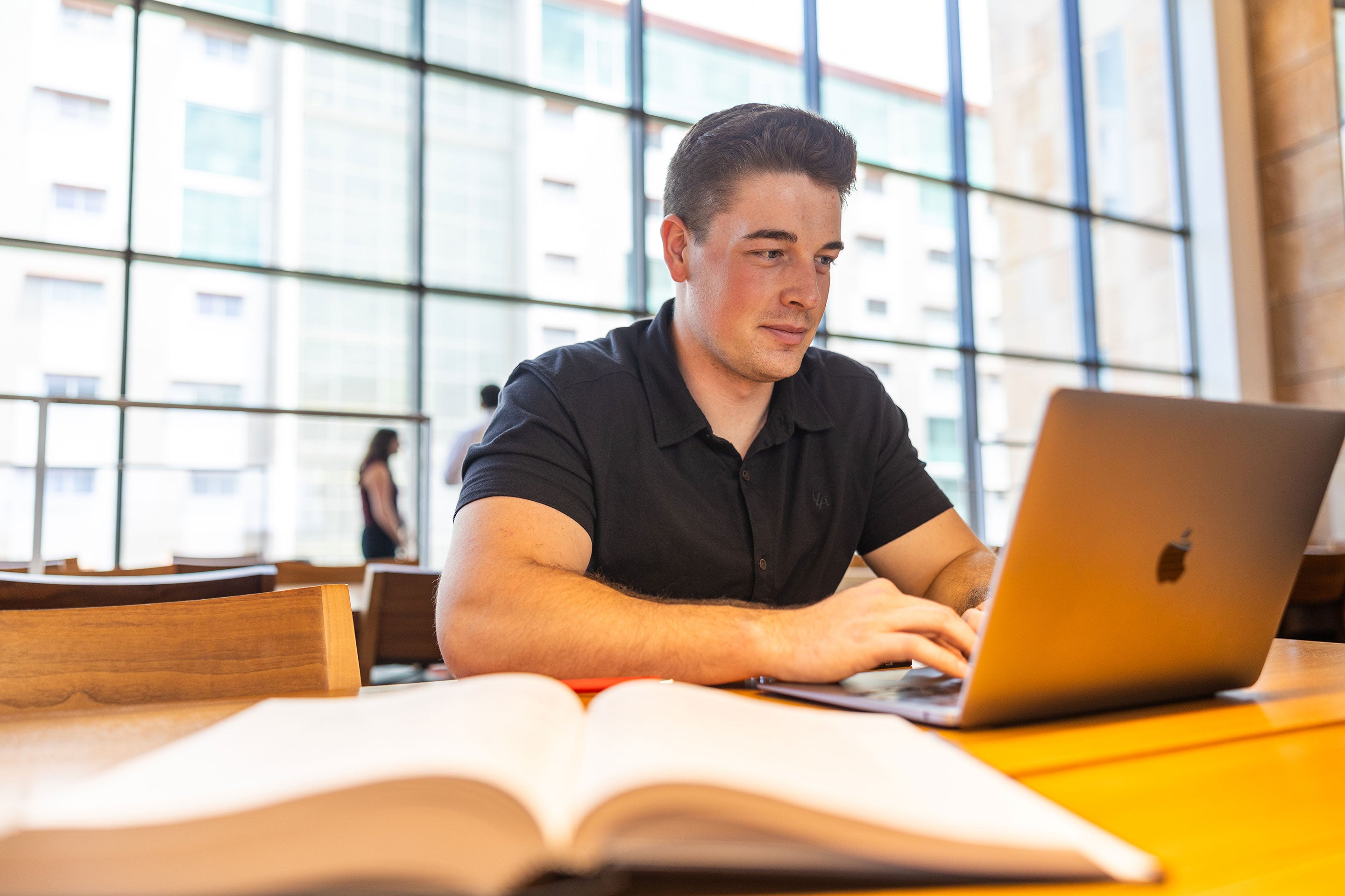 Male student sits at a table in the Sandra Day O'Connor College of Law Reading Room working on a laptop with an open book in front of him.