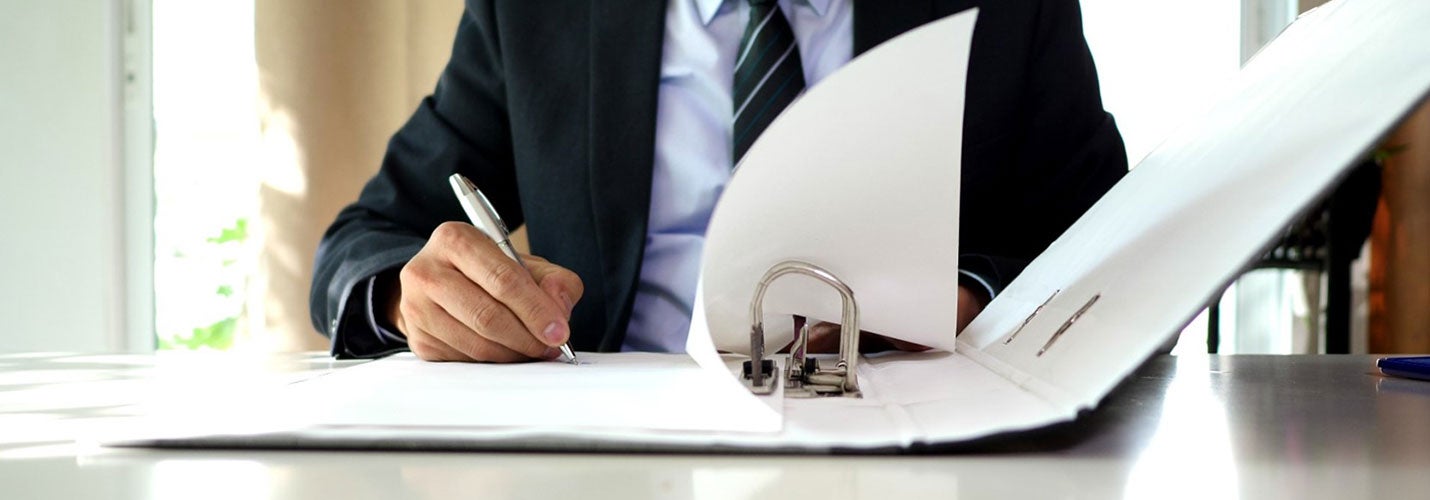 Person in suit sitting in front of a white binder signing a contract