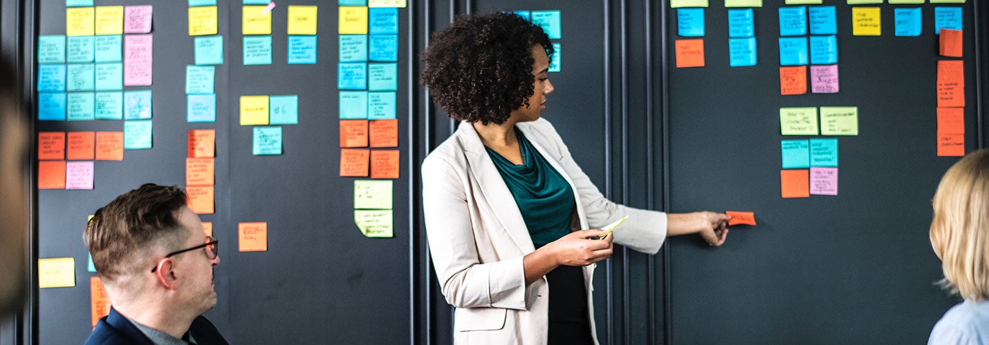 Woman standing in front of meeting putting post in notes on board