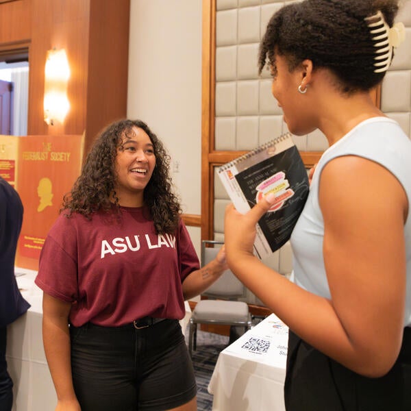 Two students engage in conversation, smiling, while attending the student organization fair.