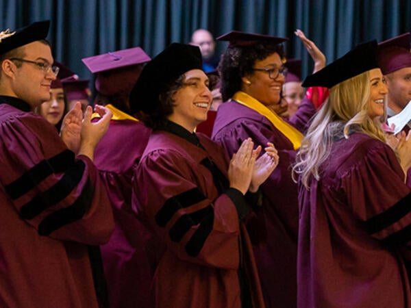 ASU Law JD and MLS graduate students in maroon regalia clapping and waving
