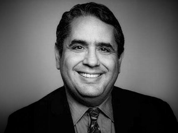 A man in a black-and-white suit smiles for the camera. 