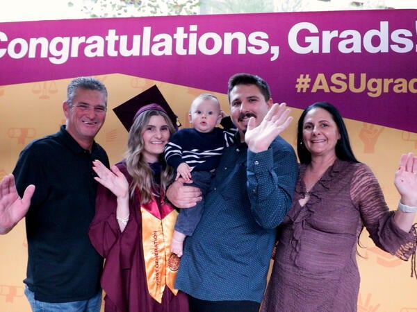 A group of graduates in maroon robes sits in folding chairs during a ceremony.