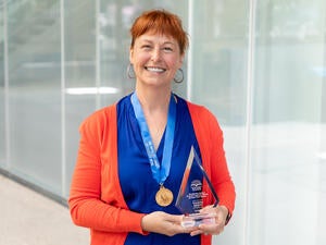 A woman in a blue blouse and orange cardigan smiles with an award.