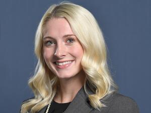 A blonde woman smiles in a grey suit.