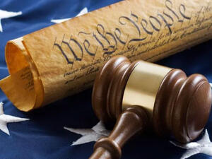 The Preamble and brown gavel laying across the blue stars on the American flag.