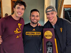 Three men in maroon and black clothing pose with a trophy.