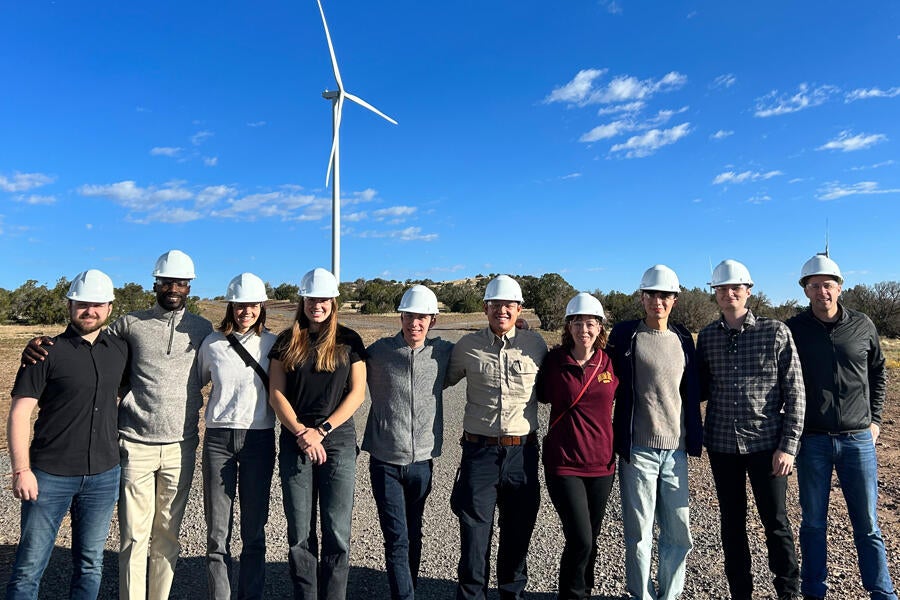 Students wearing hardhats standing outside in front of a windmill