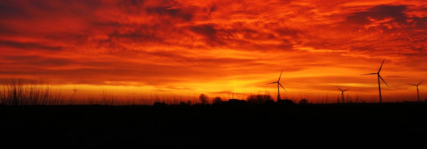 Windmills spinning in a field during a red, orange, and yellow cloudy sunset