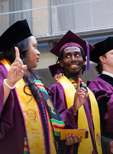 Two students attending graduation in purple and yellow robes